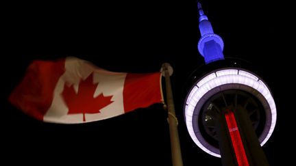 Plus haut, la&nbsp;tour CN, emblème de Toronto, au Canada,&nbsp;illuminé aux couleurs de la France,&nbsp;s'élève à côté du drapeau canadien. (CHRIS HELGREN / REUTERS)