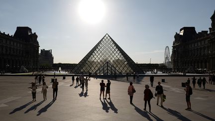 Des touristes devant la pyramide du Louvre, le 3 juillet 2019, à Paris. (LUDOVIC MARIN / AFP)