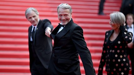 Mads Mikkelsen ne veut pas quitter le tapis rouge ! L'acteur Viggo Mortensen lui tire le bras sous le regard amusé de sa femme, Hanne Jacobsen.&nbsp; (LOIC VENANCE / AFP)