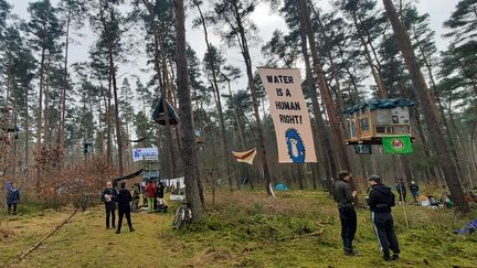 "L'eau est un droit humain", peut-on lire sur une banderole accrochée dans les arbres d'une forêt à Grünheide (Allemagne). Des militants écologistes se sont installés dans des cabanes aériennes le 29 février 2024, pour empêcher l'agrandissement d'une usine Tesla. (SEBASTIEN BAER / RADIO FRANCE)