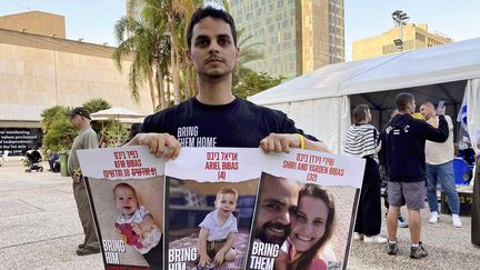 Un homme tient les portraits de proches pris en otages par le Hamas, lors des attaques du 7 octobre en Israël, le 24 novembre 2023 à Tel Aviv. (YUICHI MORII / YOMIURI / AFP)