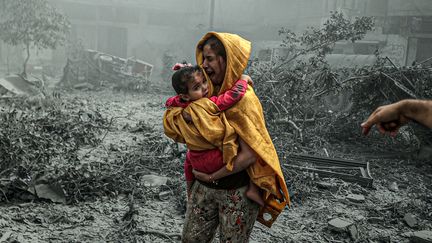 Une femme tient dans ses bras une petite fille après des frappes dans le quartier de Ridwan dans la ville de Gaza, le 23 octobre 2023. (ALI JADALLAH / ANADOLU / AFP)