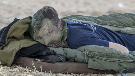 Un soldat isra&eacute;lien fait la sieste&nbsp;le visage recouvert d'une moustiquaire pr&egrave;s de la fronti&egrave;re avec la bande de Gaza (Isra&euml;l), le 8 juillet 2014. (JACK GUEZ / AFP)