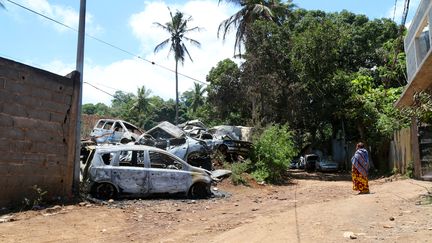 Une femme se tient devant des voitures incendiées lors de violences entre bandes, le 21 novembre 2022, à Mamoudzou (Mayotte). (GREGOIRE MEROT / AFP)