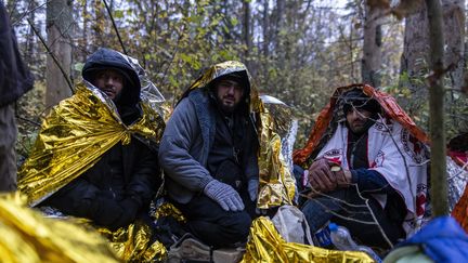 Des migrants syriens sous une couverture de survie pour se protéger du froid à Hajnowka (Pologne), à la frontière avec la Biélorussie, le 23 octobre 2021. (WOJTEK RADWANSKI / AFP)