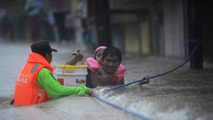 Un sauveteur aide un p&egrave;re et sa fille &agrave; avancer au milieu des forts courants, dans le village de Tumana aux Philippines, le 7 ao&ucirc;t 2012. Des pluies diluviennes s'abattent sur le pays depuis le d&eacute;but du mois.&nbsp; (TED ALJIBE / AFP)