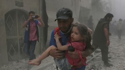 Cette enfant, secourue par cet homme, a été blessée dans l'attaque d'un centre médical du quartier Bustan el Kasr par un hélicoptère du régime, vendredi 29 avril. (BEHA EL HALEBI / ANADOLU AGENCY / AFP)