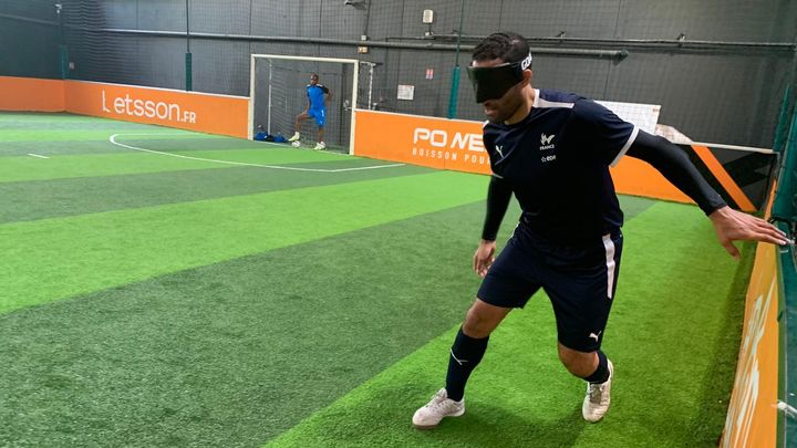 Le défenseur de l'équipe de France de cécifoot Hakim Arezki à l'entraînement à Meudon (Hauts-de-Seine), tandis qu'un membre du staff lui communique des informations depuis les cages, le 17 juin 2024. (GABRIEL JOLY / FRANCEINFO: SPORT)