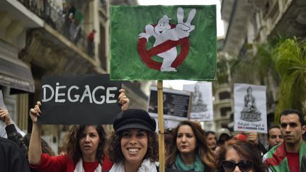 Des manifestants brandissent diverses pancartes s'adressant à&nbsp;&nbsp;Abdelaziz Bouteflika, le 8 mars, à Alger. Le logo du film "SOS Fantômes" fait référence au fait que les Algériens n'ont pas entendu la voix de leur président depuis octobre 2014. (RYAD KRAMDI / AFP)