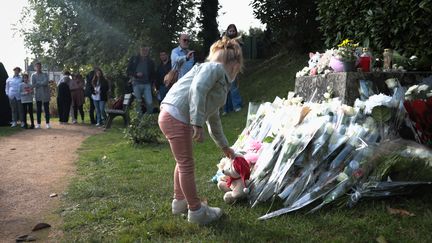 Une fillette dépose un ourson en peluche lors d'un hommage à une enfant de 3 ans tuée à Conches-en-Ouches (Eure), le 30 septembre 2023, près de la mairie de la commune. (LOU BENOIST / AFP)