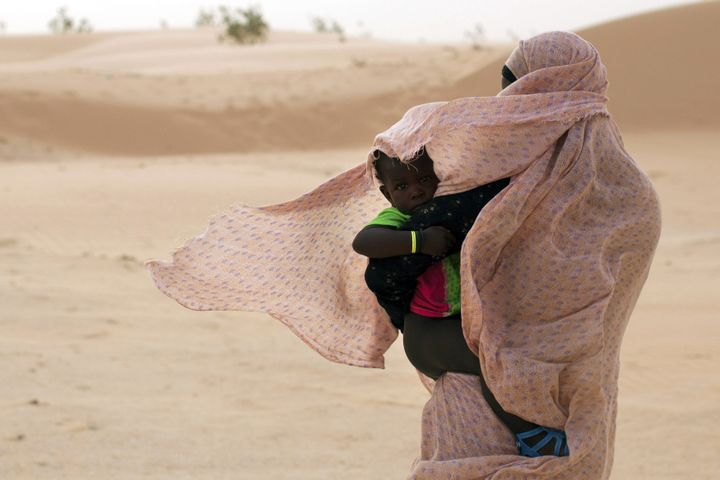 Une femme marche sur des dunes de sable à Nouakchott le 22 juin 2014, tout en protégeant son enfant contre le vent du désert. (JOE PENNEY / X02952)