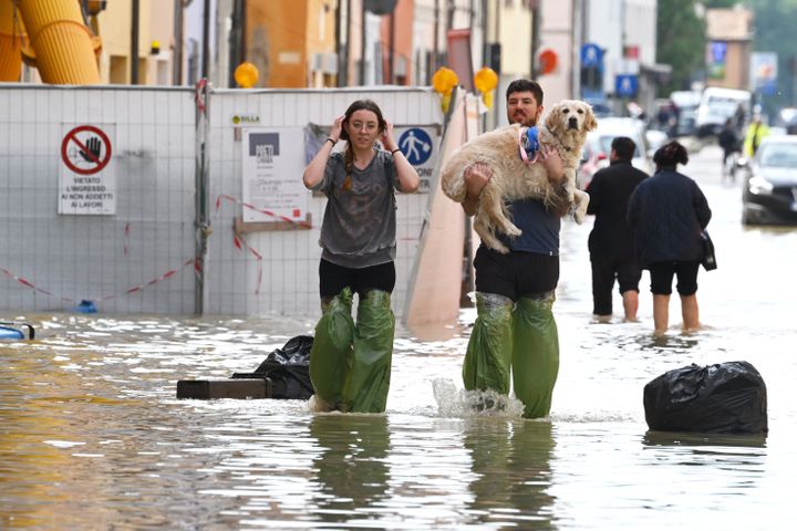 Residents carry their dog through a flooded street in Lugo, Italy, on May 18, 2023. (ANDREAS SOLARO / AFP)