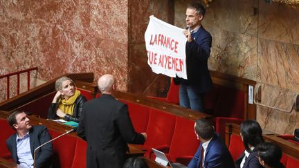 Sébastien Nadot brandit une banderole au sein de l'Hémicycle de l'Assemblée nationale, à Paris, le 19 février 2019.&nbsp; (JACQUES DEMARTHON / AFP)