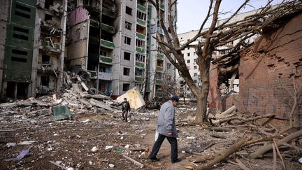 Des hommes passent devant un bâtiment résidentiel endommagé lors du bombardement d'hier dans la ville de Chernihiv, le 4 mars 2022. (DIMITAR DILKOFF / AFP)