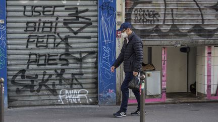 Un homme&nbsp;passe devant des magasins fermés à cause de l'épidémie de coronavirus, à Paris, le 15 mars 2020. (HERVE LEQUEUX / HANS LUCAS / AFP)