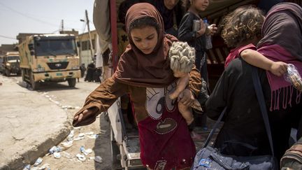 Une jeune fille irakienne, qui a fui les combats entre l'armée irakienne et l'organisation Etat Islamique (EI) dans la vieille ville de Mossoul,&nbsp;s'extirpe d'un véhicule militaire, dans le quartier industriel de la ville, le 8 juillet 2017. (FADEL SENNA / AFP)