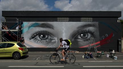 Un homme passe à vélo devant une fresque de l'artiste de rue français Rebeb représentant les yeux de la disparue Tiphaine Veron, près de la gare de Poitiers (Vienne), le 29 juillet 2021. (GUILLAUME SOUVANT / AFP)