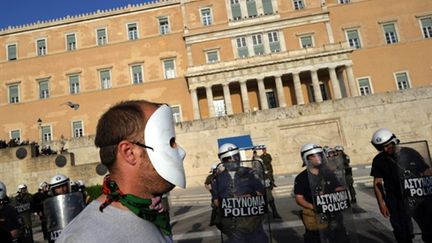 Un manifestant masqué près d'un cordon policier devant le Parlement grec à Athènes (AFP - DIMITAR DILKOFF)