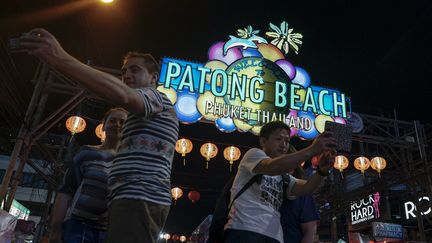 Des touristes se prennent en photo devant un panneau lumineux à Phuket (Thaïlande), le 29 mars 2016. (ATHIT PERAWONGMETHA / REUTERS)