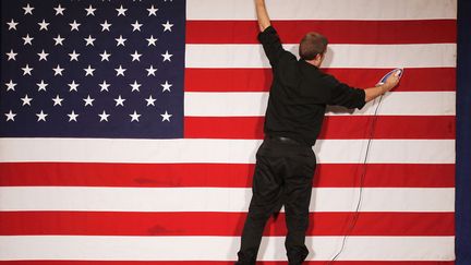 Un employ&eacute; repasse le drapeau am&eacute;ricain sur la sc&egrave;ne avant le meeting du candidat r&eacute;publicain aux primaires Mitt Romney &agrave; Des Moines (Iowa), le 3 janvier 2012. (CHIP SOMODEVILLA / GETTY IMAGES)