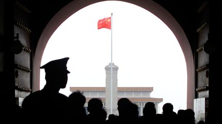 Un officier de police chinois surveille la foule qui franchit la porte nord de la place Tiananmen, à Pékin, alors que le drapeau national flotte devant le mausolée de Mao Zedong, le 13 avril 2000. (STEPHEN SHAVER / AFP)