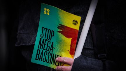 "Stop aux méga-bassines", c'est le message d'un des manifestants rassemblés le 28 novembre 2023 devant le tribunal correctionnel de Niort, en soutien aux militants écologistes jugés pour avoir organisé des rassemblements contre les "méga-bassines". (THIBAUD MORITZ / AFP)