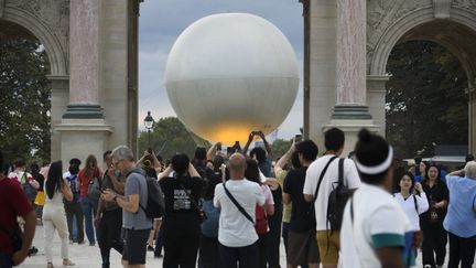 Des personnes prennent en photo la vasque olympique, devant le carrousel du Louvre à Paris, le 8 août 2024. (MAGALI COHEN / HANS LUCAS / AFP)