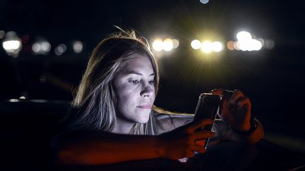 Une habitante se sert de son téléphone dans l'un des seuls lieux où il y a du réseau, à Caracas le 9 mars. (MATIAS DELACROIX / AFP)