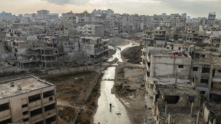 Des gens marchent au milieu des bâtiments détruits dans le centre de Homs, le 20 décembre 2024, en Syrie. (SAMEER AL-DOUMY / AFP)