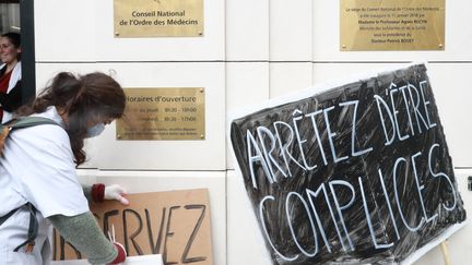 Une militante féministe dépose une pancarte devant le Conseil national de l'Ordre des médecins, lundi 18 mars.&nbsp; (JACQUES DEMARTHON / AFP)