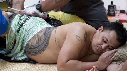 Le maître tatoueur Su'a Paul Sulu'ape est aidé par deux assistants qui tendent la peau de Ricky Masoe. (AFP PHOTO / MARTY MELVILLE)