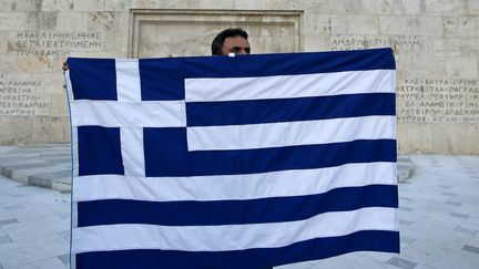 Un manifestant brandit un drapeau grec devant le b&acirc;timent du Parlement, &agrave; Ath&egrave;nes (Gr&egrave;ce), le 13 juillet 2015. (JEAN-PAUL PELISSIER / REUTERS)