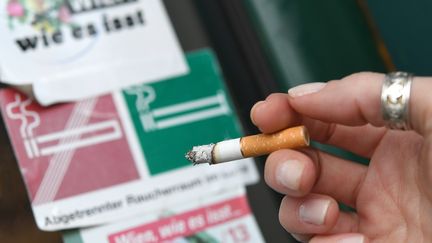 Une cigarette allumée entre les doigts d'un fumeur à Vienne, en Autriche. (HELMUT FOHRINGER / APA-PICTUREDESK)