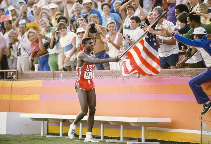 Le sprinteur américain Carl Lewis attrape un drapeau tendu par un spectateur, après sa victoire sur le 100 m aux JO de Los Angeles (Etats-Unis), le 4 août 1984. (DAVID MADISON / GETTY IMAGES NORTH AMERICA)