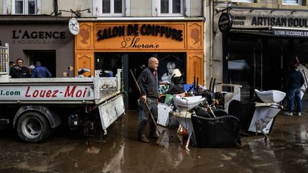 Un homme nettoie la boue et les meubles endommagés par les inondations à l’extérieur d’une boutique dans une rue de la ville d’Annonay (Ardèche), le 18 octobre 2024. (JEFF PACHOUD / AFP)