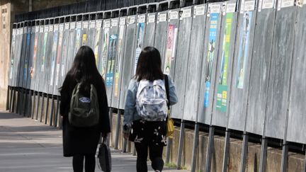 Deux femmes passent devant des panneaux électoraux&nbsp;installés pour les élections européennes, le 22 mai 2019, à Paris. (LUDOVIC MARIN / AFP)