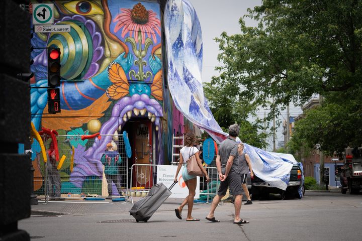 Des gens regardent des artistes au travail pendant le festival de la murale à Montréal, au Québec, le 16 juin 2022.&nbsp; (PAOLA CHAPDELAINE / AFP)