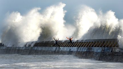 Malgré l'alerte orange, le 8 février 2016, deux personnes s'aventurent sur une digue pour exécuter des figures au milieu des vagues. (FRED TANNEAU / AFP)