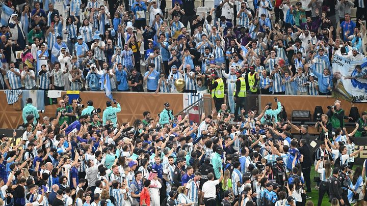 Porté en triomphe par ses coéquipiers, suivi par une nuée de photographes, Lionel Messi présente la Coupe du monde aux supporters argentins présents à Doha. C'est lui qu'on distingue (à peine) dans la foule, juste en-dessous des stadiers en gilets jaunes. (ERCIN ERTURK / ANADOLU AGENCY / AFP)