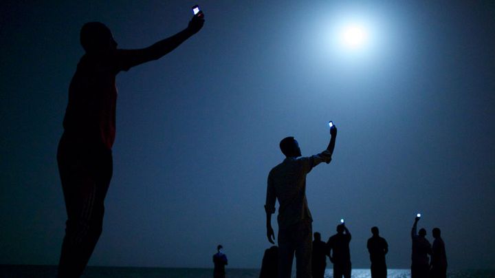 Des migrants africains brandissent leurs t&eacute;l&eacute;phones sur une plage de Djibouti, f&eacute;vrier 2013. (JOHN STANMEYER / VII FOR NATIONAL GEOGRAPHIC)