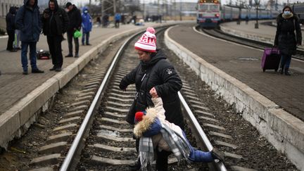 Une mère aide son enfant à traverser une voie de chemin de fer à la gare de Lviv, en Ukraine, le 4 mars 2022. Plus d'1 million 200 000 personnes ont fui l'Ukraine&nbsp;vers les pays voisins, depuis le déclenchement de l'invasion russe, le 24 février 2022. (DANIEL LEAL / AFP)