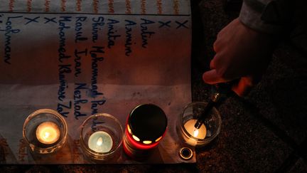 Une femme allume des bougies pour éclairer une pancarte égrénant le nom de migrants morts en tentant de traverser la Manche, parc de Richelieu à Calais (Pas-de-Calais), le 25 novembre 2021. (MOHAMMED BADRA / EPA)