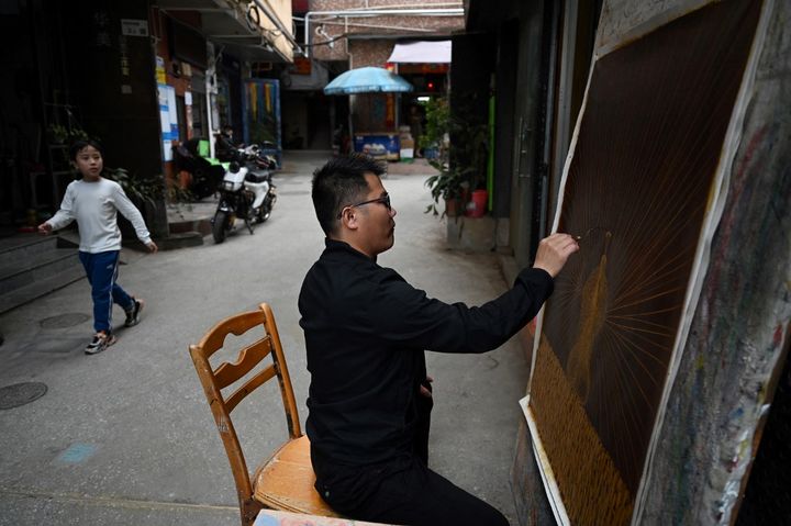 L'artiste Wu Feimin en pleine création dans une ruelle de Dafen. (GREG BAKER / AFP)