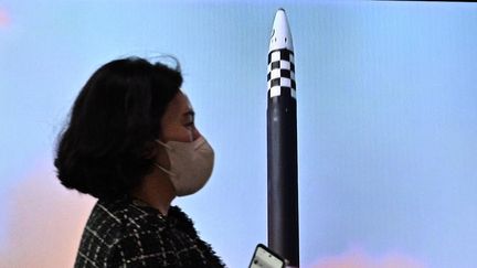 Une femme passe devant un écran projetant un reportage télévisé montrant des images d'archives d'un essai de missile nord-coréen, dans une gare à Séoul, le 6 octobre 2022. (ANTHONY WALLACE / AFP)