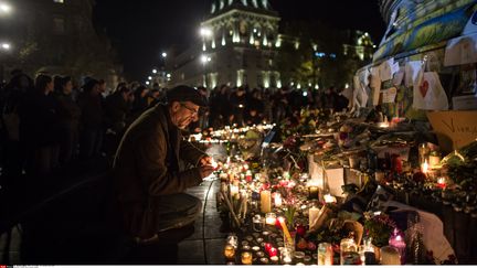 Un homme dépose une bougie sur un mémorial improvisé en mémoire des victimes des attentats, place de la République, à Paris, le 15 novembre 2015. (GEAI LAURENCE / SIPA)