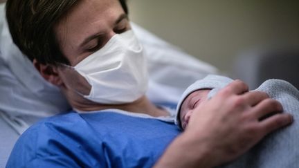 Un père tient son fils peu après sa naissance, le 17 novembre 2020, à la maternité des Diaconesses, à Paris. (MARTIN BUREAU / AFP)