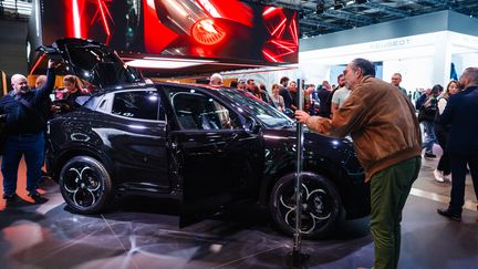 Des visiteurs du Mondial de l'auto à Paris observent un modèle hybride d'Alfa Romeo, le 15 octobre 2024. (DIMITAR DILKOFF / AFP)