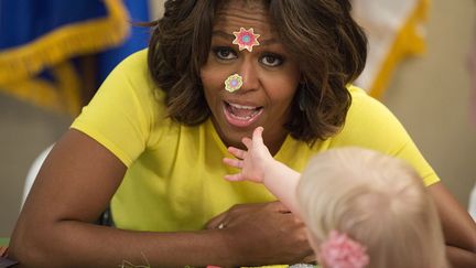 La First Lady Michelle Obama re&ccedil;oit des autocollants &agrave; la figure lanc&eacute;s par une petite fille de 20 mois alors qu'elle visite un centre de soins pour jeunes enfants &agrave; Bethesda (Maryland, Etats-Unis), le 14 avril 2014. (JOSHUA ROBERTS / REUTERS)