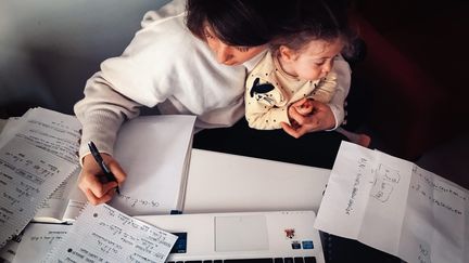 Une femme travaille avec son enfant dans les bras. (photo d'illustration) (FRANCESCO ALGERI / MAXPPP)