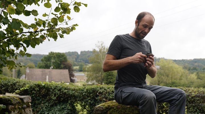 Assis sur un muret, Mathias Dolidon cherche à capter le réseau mobile à Brassy (Nièvre). (PIERRE-LOUIS CARON / FRANCEINFO)